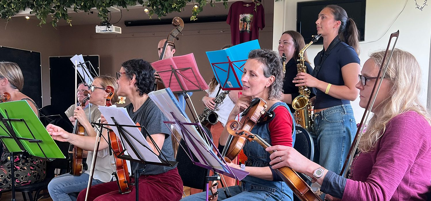 Image of group of musicians with violin players in foreground and saxophone and double bass players in background