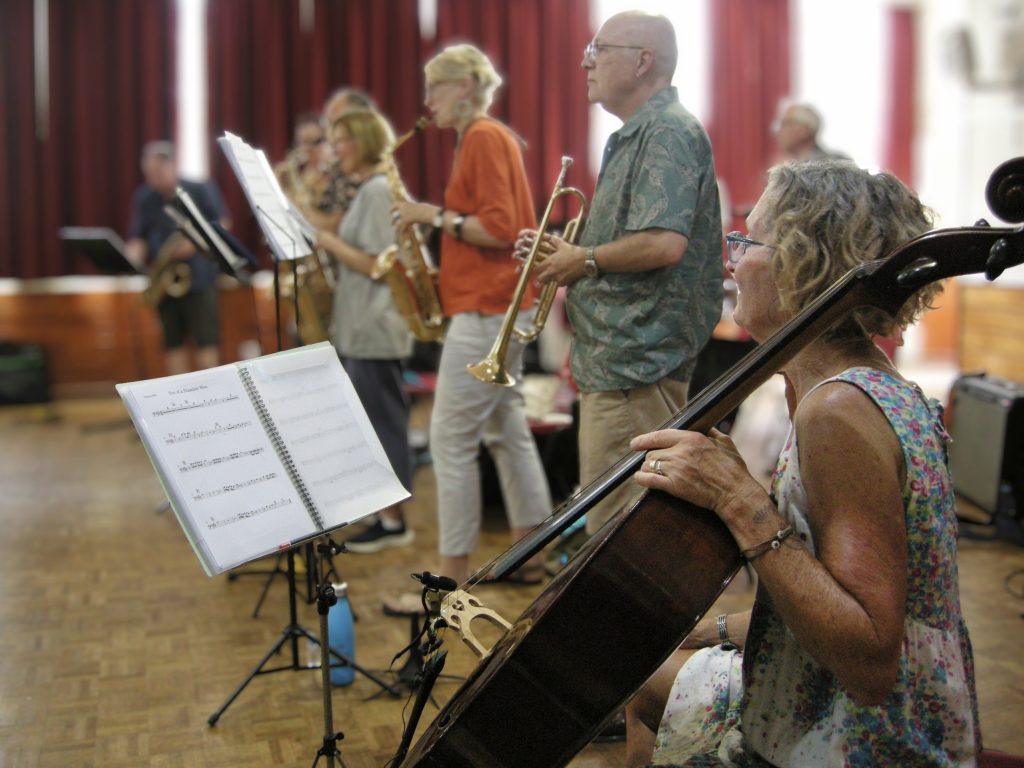 Female cello player in foreground with brass players in background