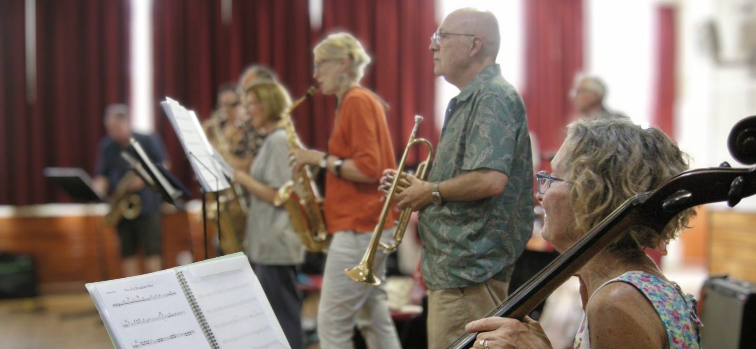 Female cello player in foreground with brass players in background