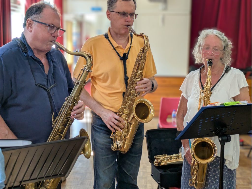 Three people playing tenor saxophones two men on left and one woman on right