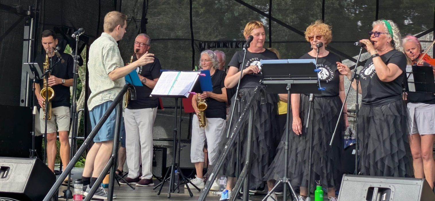 Soul Collective performance at Proms in the Park 2026, Saxophonist on right, conductor, singers on right.